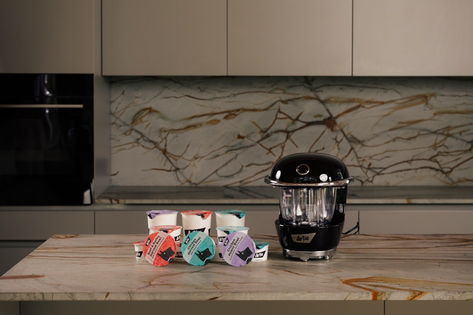 Black kitchen appliance on a marble countertop with colorful packets in the background