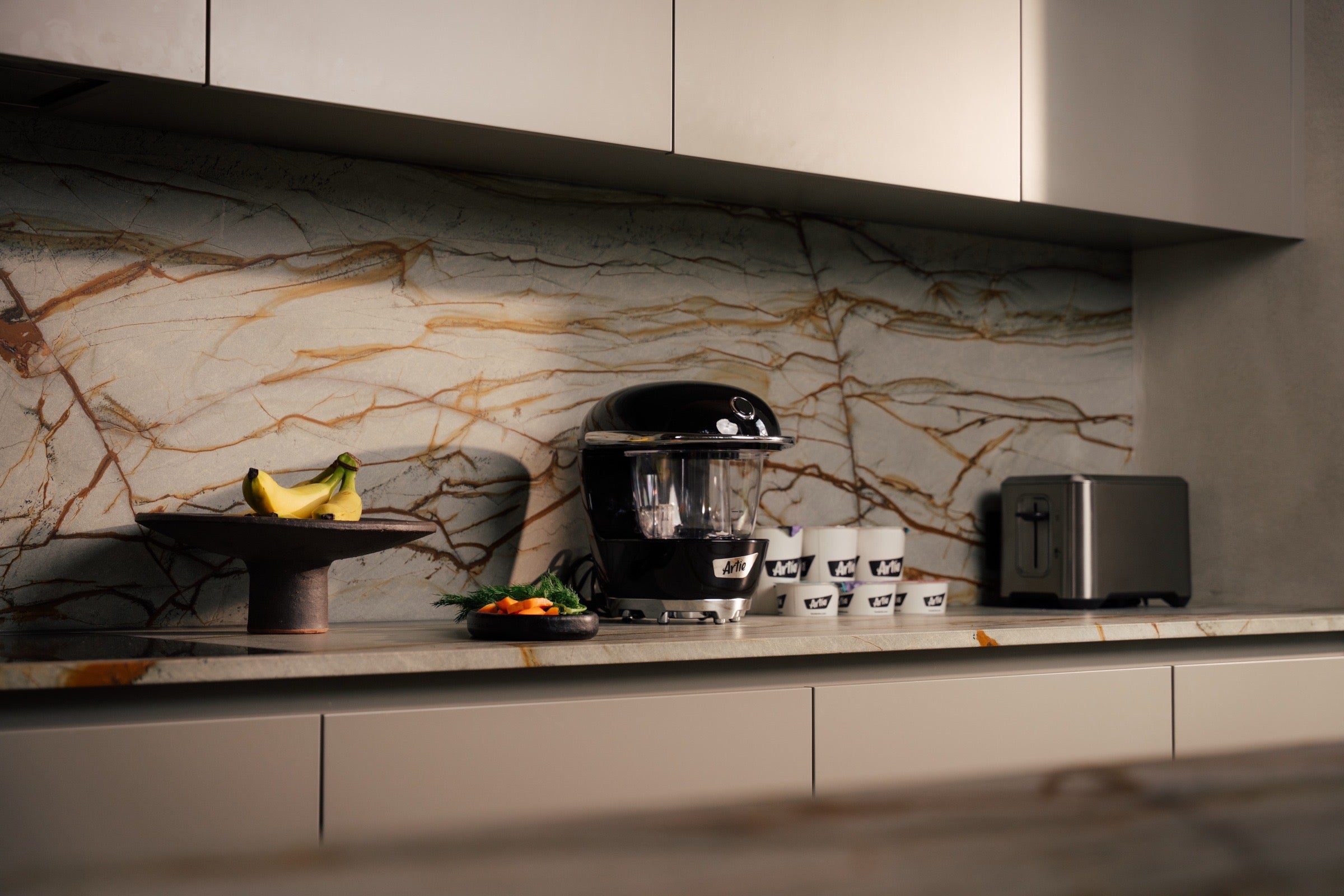 Modern kitchen with marble backsplash, appliances, and a fruit bowl.